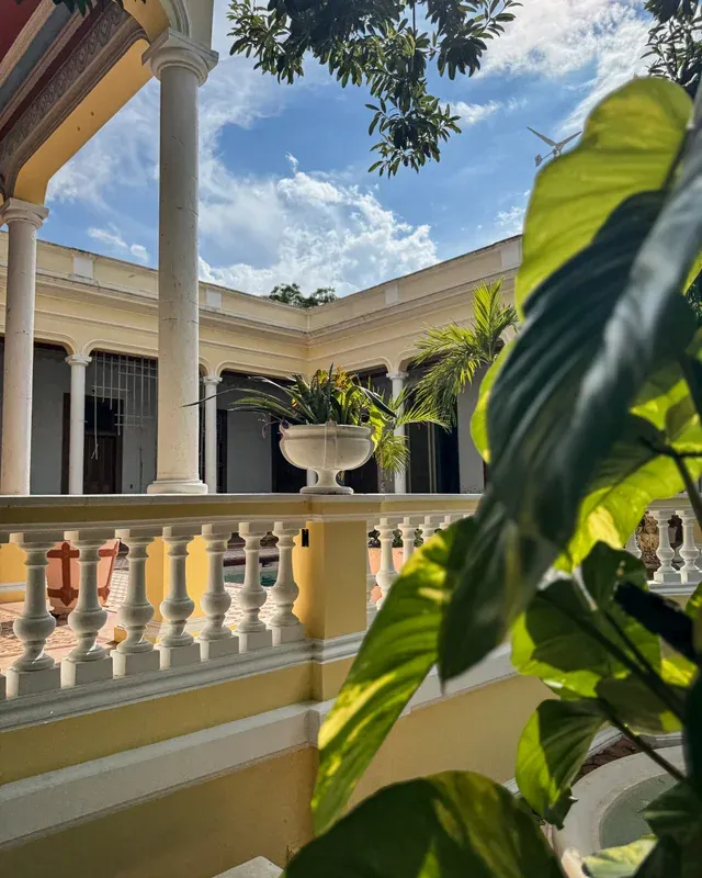 Corredor de columnas y balaustrada alrededor del patio, con macetón de palmeras